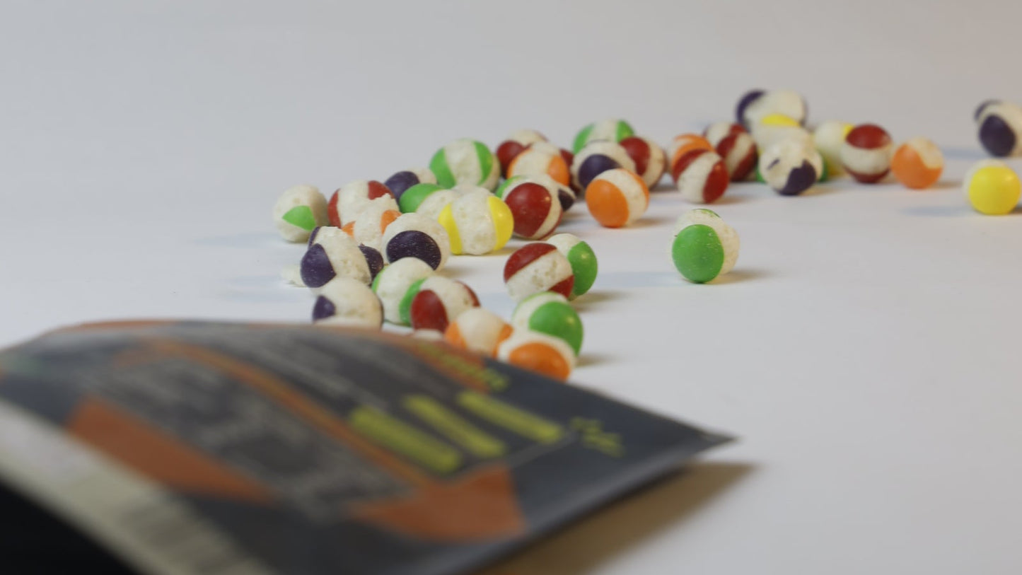 Colorful candy pieces on a white surface with a blurred package in the foreground.