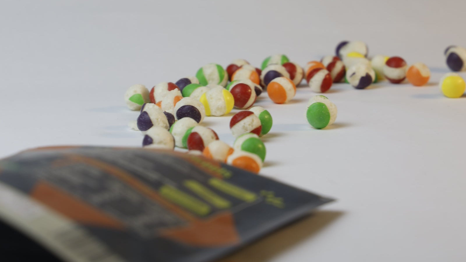 Colorful candy pieces on a white surface with a blurred package in the foreground.